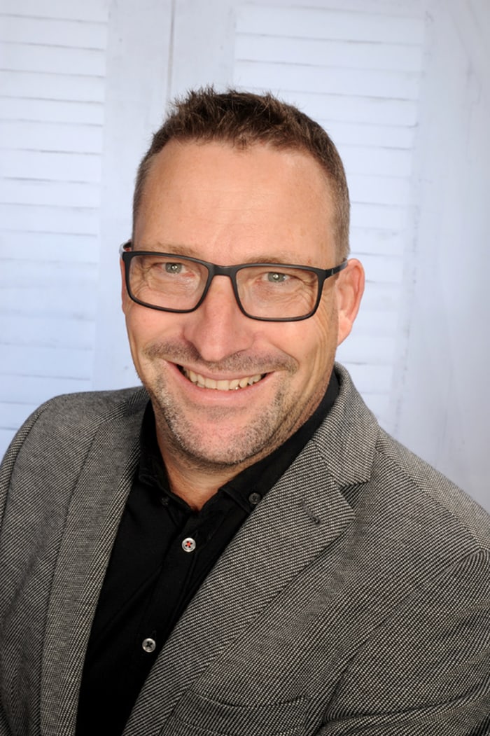 Ein lächelnder Bautechniker mit Brille und grauem Sakko.